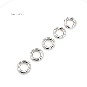 May include: Five silver-toned metal rings arranged in a diagonal line. Each ring features a smooth, rounded surface and a small stamp with the letters PG on the top edge. The text Five Per Pack is printed in black in the upper left corner.