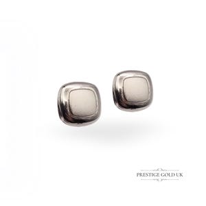 May include: Two silver-toned square stud earrings with a rounded shape and a light-colored center. The earrings are displayed against a white background, showcasing their polished finish and minimalist design. The earrings are a jewelry item.