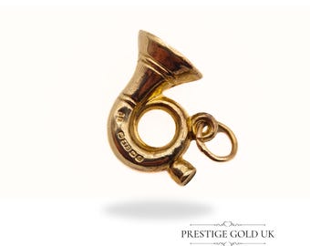 May include: A gold-colored musical instrument charm in the shape of a French horn. The charm has a loop for attaching to a necklace or bracelet. The charm is marked with the inscription "9ct 375".