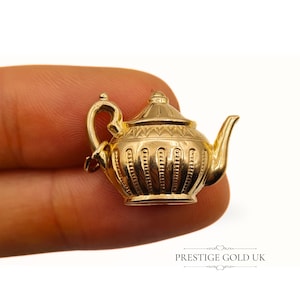 May include: A gold-colored teapot charm with intricate details. The charm is made of metal and has a shiny finish.