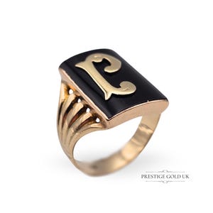 May include: A gold ring with a black enamel rectangular top featuring a gold letter 'L'.