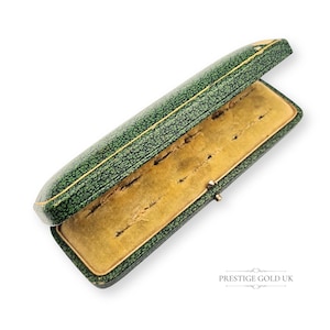 Pode incluir: Uma caixa de joias verde vintage aberta, com um exterior texturizado e um interior dourado. A caixa é retangular e tem uma tampa articulada. O interior é forrado com um tecido macio amarelo.
