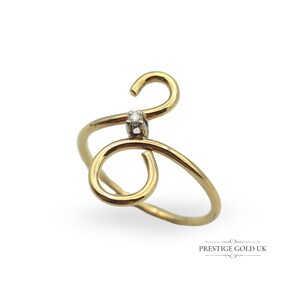 May include: A gold ring with a single diamond set in the center. The ring is designed in a swirling, abstract shape.