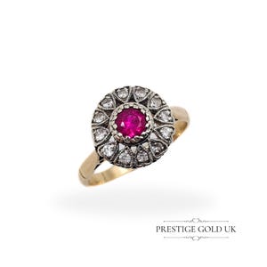 May include: A gold ring featuring a ruby centre stone surrounded by a halo of smaller diamonds. The ring is set in a vintage style.