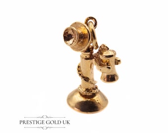 May include: A gold-colored charm in the shape of a vintage rotary phone. The phone has a detailed design with a receiver and a base.
