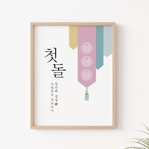 May include: A framed print with a pink, blue, and yellow design. The print features Korean calligraphy that reads "Cheotdeul" and a quote in Korean. The print is in a light wood frame.
