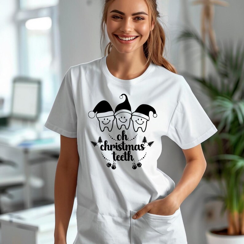 May include: White t-shirt featuring a graphic of three smiling teeth wearing Santa hats. The text "oh christmas teeth" is below the teeth. The design includes small Christmas trees and ornaments. The shirt is a short-sleeved crew neck.