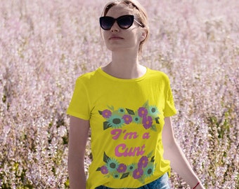 Może przedstawiać: Żółty t-shirt z kwiatowym wzorem i różowym napisem "I'm a Cunt". Koszulka jest połączona z niebieskimi dżinsami. Osoba nosi okulary przeciwsłoneczne i stoi na polu fioletowych kwiatów.