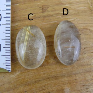 May include: Two oval-shaped, clear quartz stones with gold inclusions. The stones are about 2 inches long and are labeled "C" and "D".