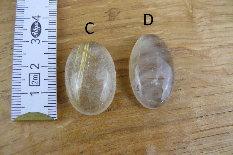 May include: Two oval-shaped, clear quartz stones with gold inclusions. The stones are about 2 inches long and are labeled "C" and "D".