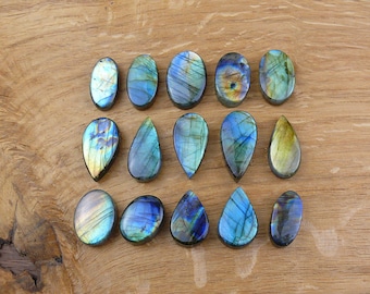 May include: A collection of 16 iridescent labradorite gemstone cabochons in teardrop shapes. The stones are a mix of blue, green, and gold colors.
