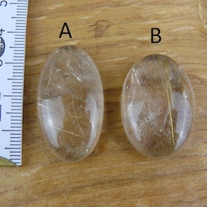 May include: Two oval-shaped clear quartz stones with gold inclusions. The stones are labeled "A" and "B".