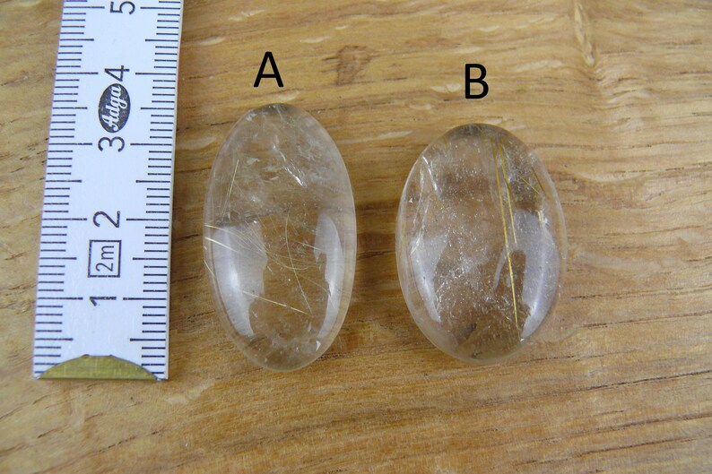 May include: Two oval-shaped clear quartz stones with gold inclusions. The stones are labeled "A" and "B".