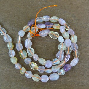 May include: A strand of light pink, yellow, and purple gemstone beads. The beads are smooth and oval-shaped. The beads are strung on a thin orange thread.
