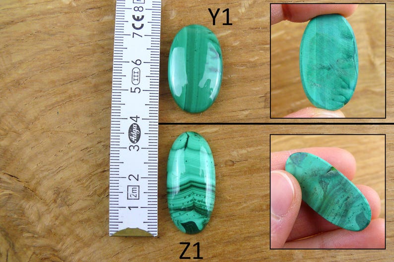 May include: Two oval-shaped malachite gemstones, one with a solid green color and the other with banded patterns. A ruler shows the stones' length. The gemstones are displayed on a wooden surface.