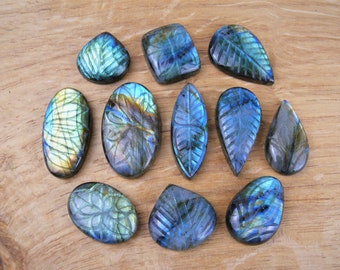 May include: Twelve iridescent blue-green labradorite gemstone cabochons carved with leaf designs. The cabochons are various shapes and sizes, including oval, teardrop, and square.