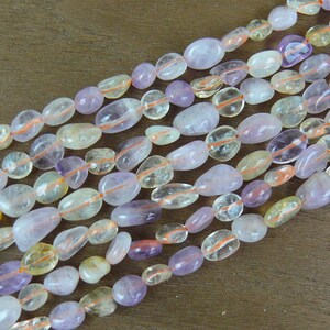 May include: A strand of smooth, oval-shaped gemstone beads in shades of light purple, yellow, and white. The beads have a translucent appearance and are strung together on a clear thread.