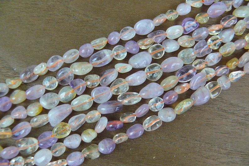 May include: A strand of smooth, oval-shaped gemstone beads in shades of light purple, yellow, and white. The beads have a translucent appearance and are strung together on a clear thread.