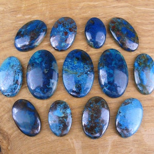 Peut inclure: Une collection de pierres précieuses ovales dans des tons de bleu et de brun. Les pierres polies de tailles variables sont disposées sur une surface en bois brun clair. Les pierres ont une finition brillante et présentent des motifs naturels.