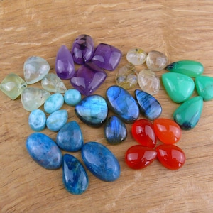 May include: Assortment of colourful gemstone cabochons in various shapes and sizes, including amethyst, labradorite, aquamarine, and carnelian.