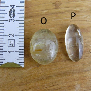 May include: Two oval-shaped clear quartz stones with gold inclusions, labeled "O" and "P", next to a ruler measuring 1 to 4 centimeters.