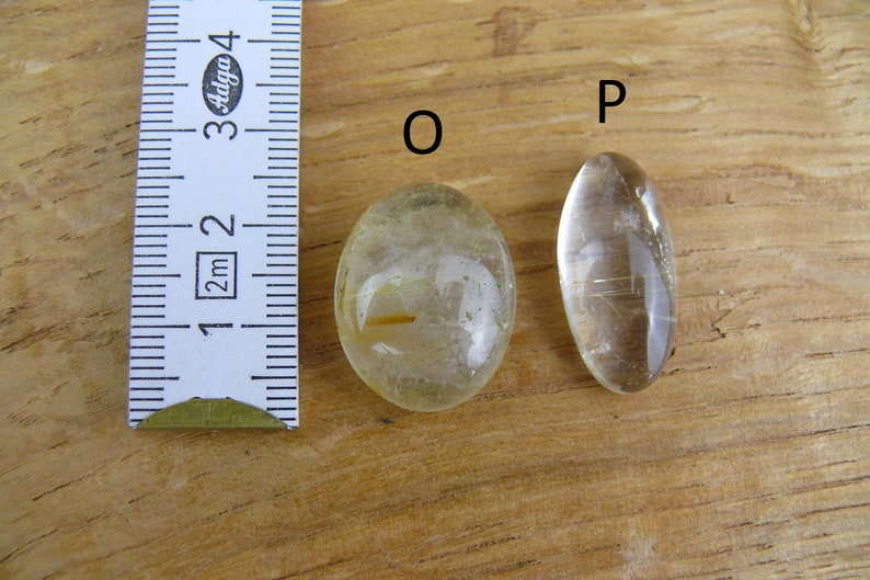 May include: Two oval-shaped clear quartz stones with gold inclusions, labeled "O" and "P", next to a ruler measuring 1 to 4 centimeters.