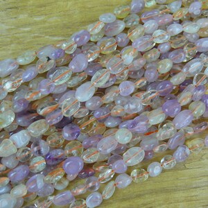 May include: A strand of mixed gemstone beads, featuring a mix of light purple, clear, and yellow-orange stones. The beads are oval-shaped and have a smooth, polished finish.