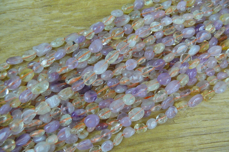 May include: A strand of mixed gemstone beads, featuring a mix of light purple, clear, and yellow-orange stones. The beads are oval-shaped and have a smooth, polished finish.