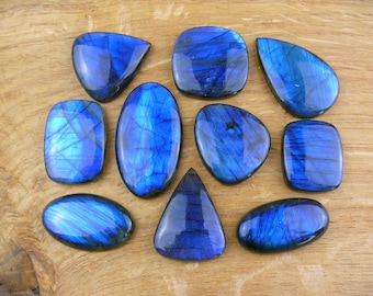 May include: Assortment of ten blue labradorite gemstone cabochons of various shapes and sizes. The cabochons are arranged on a wooden surface.