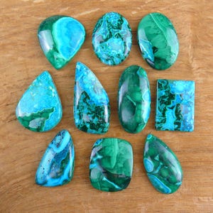 Può includere: Una collezione di dieci pietre preziose levigate in varie forme, tra cui goccia, ovale e rettangolare. Queste pietre presentano vortici e motivi vibranti di verde bosco profondo, turchese brillante e inclusioni minerali blu cielo.