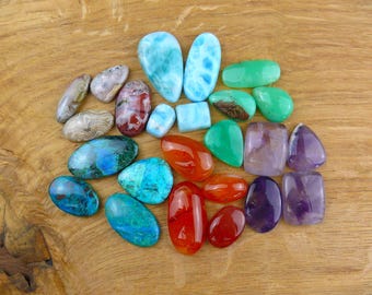 May include: A collection of polished gemstones in various shapes and sizes, including blue larimar, green chrysoprase, orange carnelian, purple amethyst, and blue-green azurite-malachite, all featuring smooth, rounded surfaces and vibrant colors.