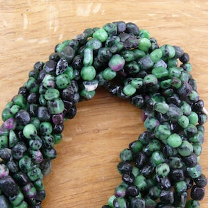 Könnte beinhalten: Eine Strähne aus grünen und schwarzen Edelsteinperlen. Die Perlen sind unregelmäßig geformt und haben eine glatte, polierte Oberfläche.