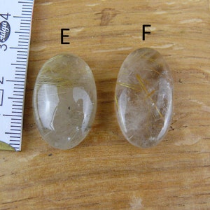 May include: Two oval-shaped clear quartz stones with gold inclusions. The stones are labeled "E" and "F".