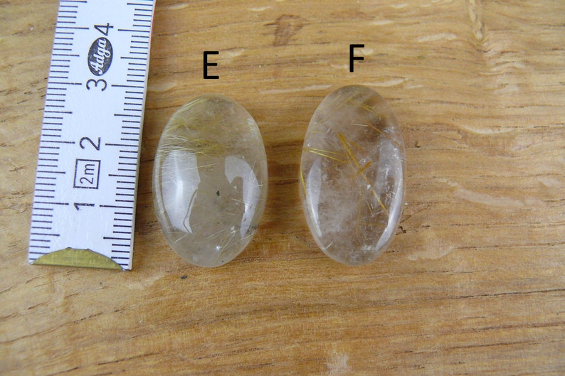 May include: Two oval-shaped clear quartz stones with gold inclusions. The stones are labeled "E" and "F".