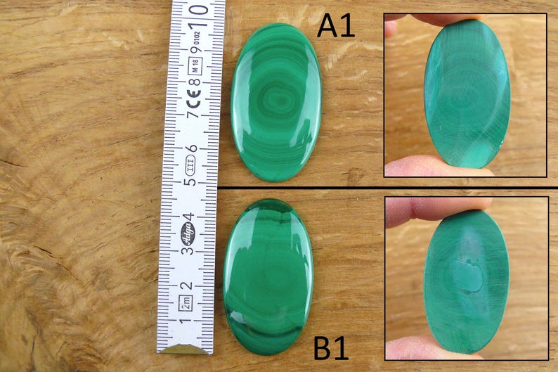 May include: Two polished oval malachite gemstones, one labeled A1 and the other B1, are displayed. The gemstones are a vibrant green with unique swirling patterns. A ruler shows the approximate size of the stones.