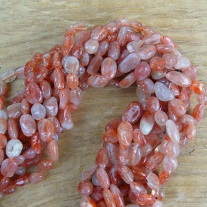 Può includere: Una collana di perle di pietra di sole rotonde in tonalità arancio e rosso. Le perle sono lisce e lucidate, con una forma naturale irregolare.