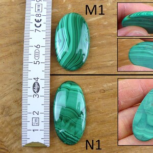 May include: Two oval-shaped malachite stones with green and dark green patterns. The stones are next to a ruler showing measurements in centimeters. Additional images show the stones from different angles, highlighting their polished surfaces.