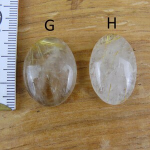May include: Two oval-shaped clear quartz stones with gold inclusions. The stones are labeled "G" and "H".