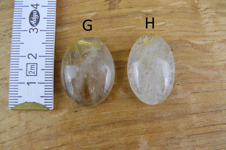 May include: Two oval-shaped clear quartz stones with gold inclusions. The stones are labeled "G" and "H".