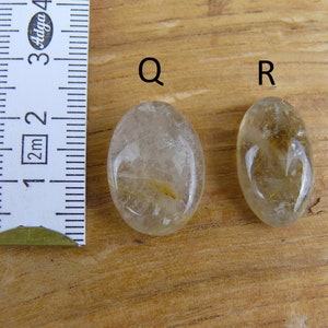 May include: Two oval-shaped clear quartz stones with gold inclusions. The stones are labeled "Q" and "R". A ruler is in the background.