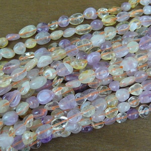 May include: A strand of mixed gemstone beads, featuring a mix of light purple amethyst, clear quartz, and yellow citrine beads. The beads are smooth and oval-shaped, and they are strung on a clear elastic cord.