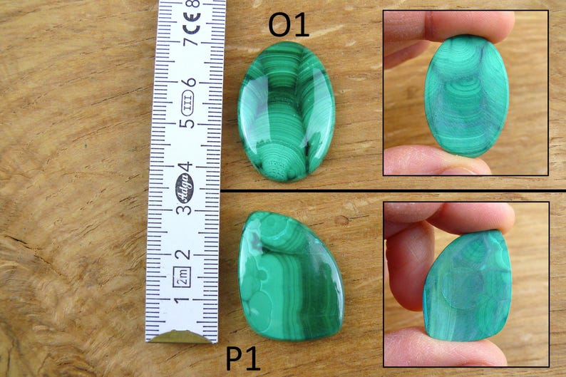 May include: Two polished malachite gemstones, one oval and one irregularly shaped, displayed on a wooden surface. The oval stone is approximately 2 inches long. The malachite has a vibrant green color with swirling patterns. A ruler is placed next to the stones.