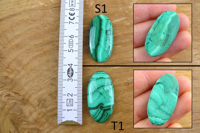 May include: Two oval-shaped malachite stones with green and black patterns. One stone is labeled "S1" and the other "T1". A ruler is placed next to the stones, showing measurements in centimeters. The stones are displayed on a wooden surface.