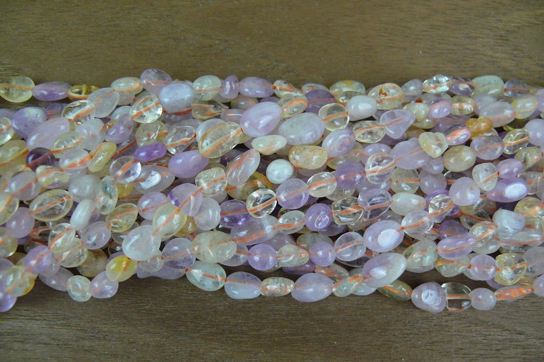 May include: A strand of mixed gemstone beads, featuring a mix of light purple, clear, and yellow beads. The beads are smooth and oval-shaped.