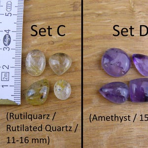 May include: Two sets of gemstone cabochons. Set C features four rutilated quartz cabochons in shades of yellow and gold, measuring 11-16 mm. Set D features four amethyst cabochons in shades of purple, measuring 15-17 mm.