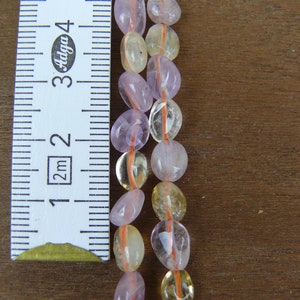 May include: Two strands of beads, one strand is light pink and the other is light yellow. The beads are oval shaped and are strung on a thin orange thread. A ruler is in the background to show the size of the beads.