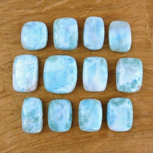Könnte beinhalten: Zwölf rechteckige, polierte Larimar-Edelsteine in verschiedenen Blau- und Weißtönen, angeordnet auf einer Holzoberfläche. Jeder Stein hat ein einzigartiges Muster, das die natürliche Schönheit des Minerals zeigt.