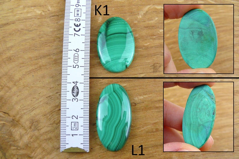 May include: Two oval-shaped malachite gemstones with a vibrant green color and distinctive banded patterns. One gemstone is shown next to a ruler, and two others are held by a person. The gemstones are approximately 2 inches in length.