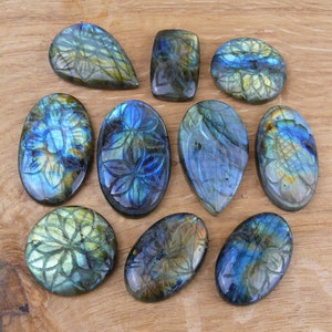 Può includere: Assortimento di 10 cabochon di labradorite intagliata con colori iridescenti blu, verdi e dorati. I cabochon sono di forma ovale e a goccia e presentano motivi floreali.