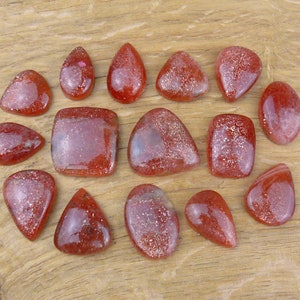 Peut inclure: Assortiment de 14 cabochons de pierre de soleil rouge avec une finition chatoyante et irisée. Les cabochons sont de formes et de tailles variées, notamment en forme de larme, ovale et carré.